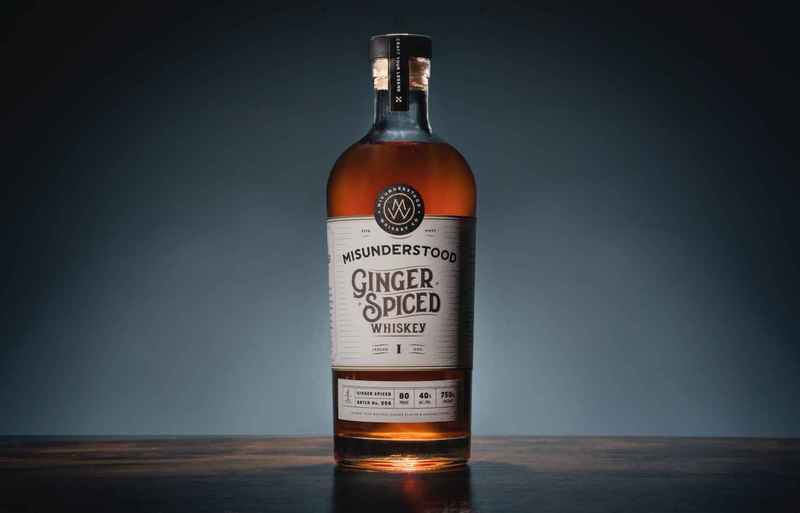Bottle of flavored spirit labeled Misunderstood Ginger Spiced Whiskey against a slate gray background.