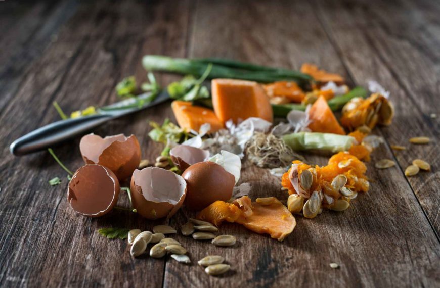 Food scraps including squash pieces, seeds, eggshells, and green onions on wooden table with a knife.