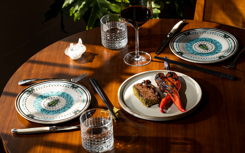 A table set with colorful plates, wine and water glasses, chopsticks, and a dish of Wagu short ribs at Koko Ni restaurant in Denver, Colorado.