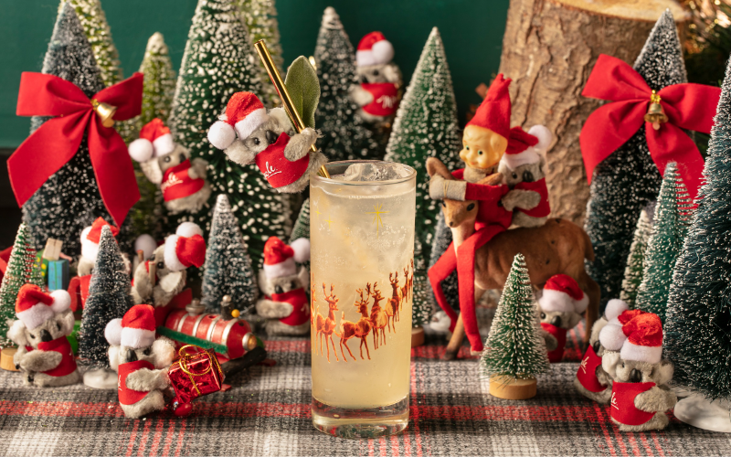A cocktail in a high-ball glass featuring reindeer amid a Christmas scene with Christmas trees and koalas 