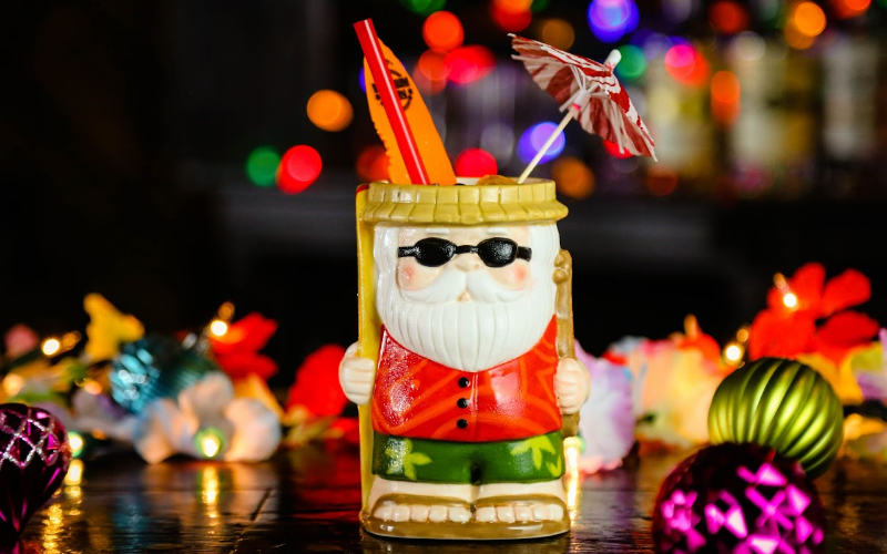 A cocktail served in a mug shaped like Santa Claus wearing surf shorts in a festive setting