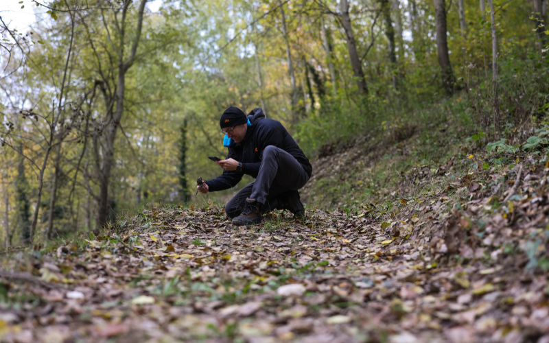 A Man is kneeling to take a picture in the woods during a truffle hunt for Denver's Restaurant Olivia 