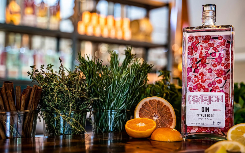 bar with fresh herbs in glass and pink bottle of gin and orange