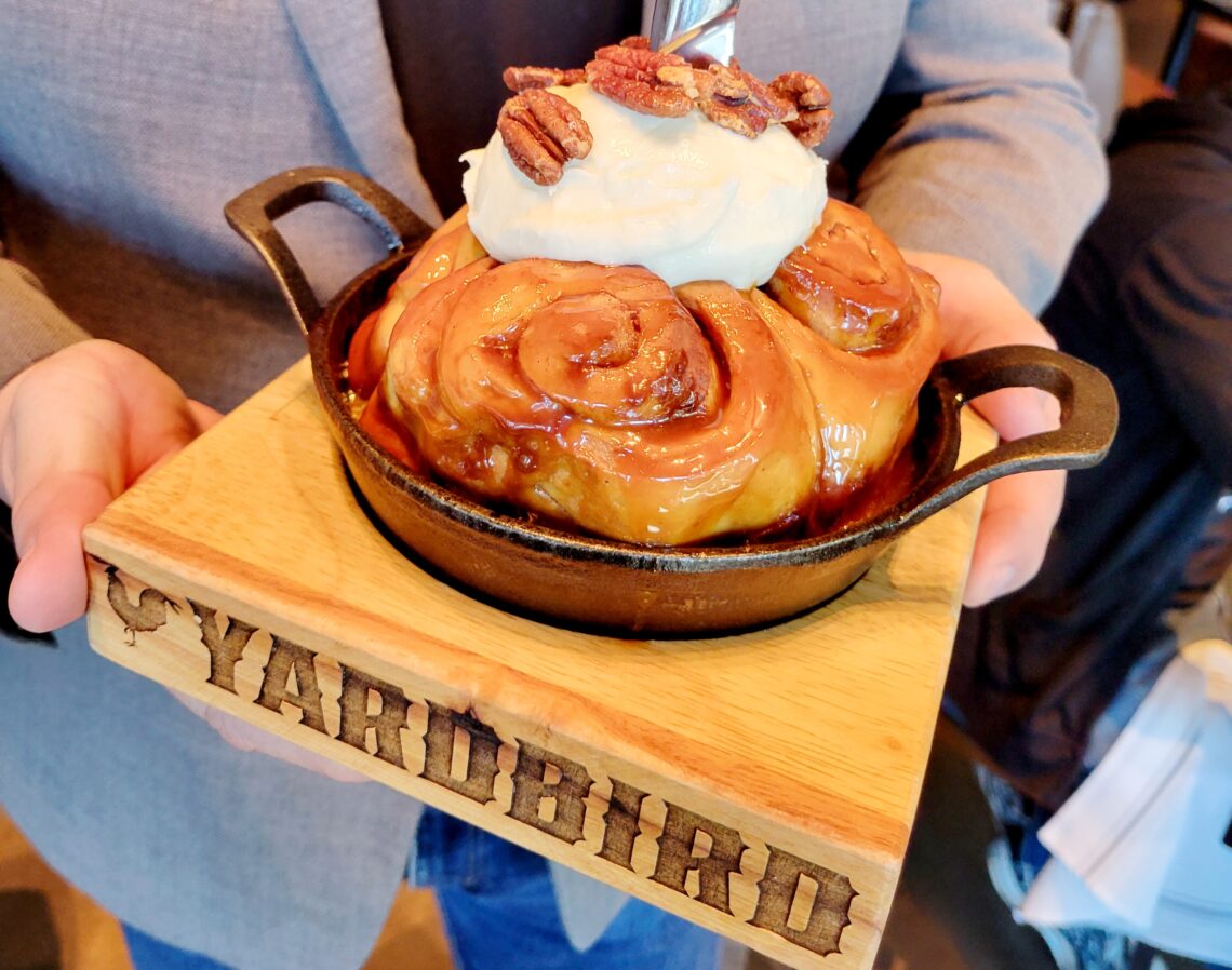 wood board with cinnamon roll in skillet