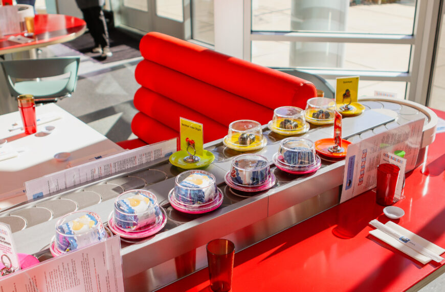red booths with sushi in covered dishes on conveyor belt