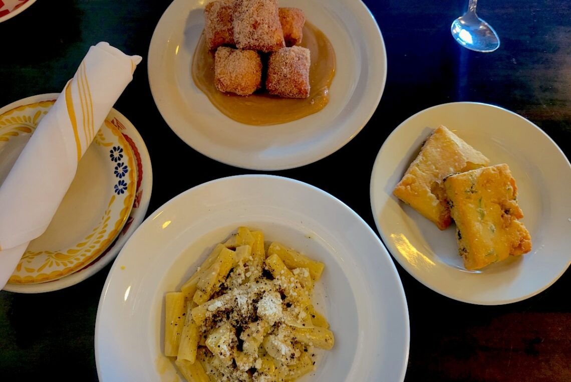table with four white plates and pasta, fritters and a napkin