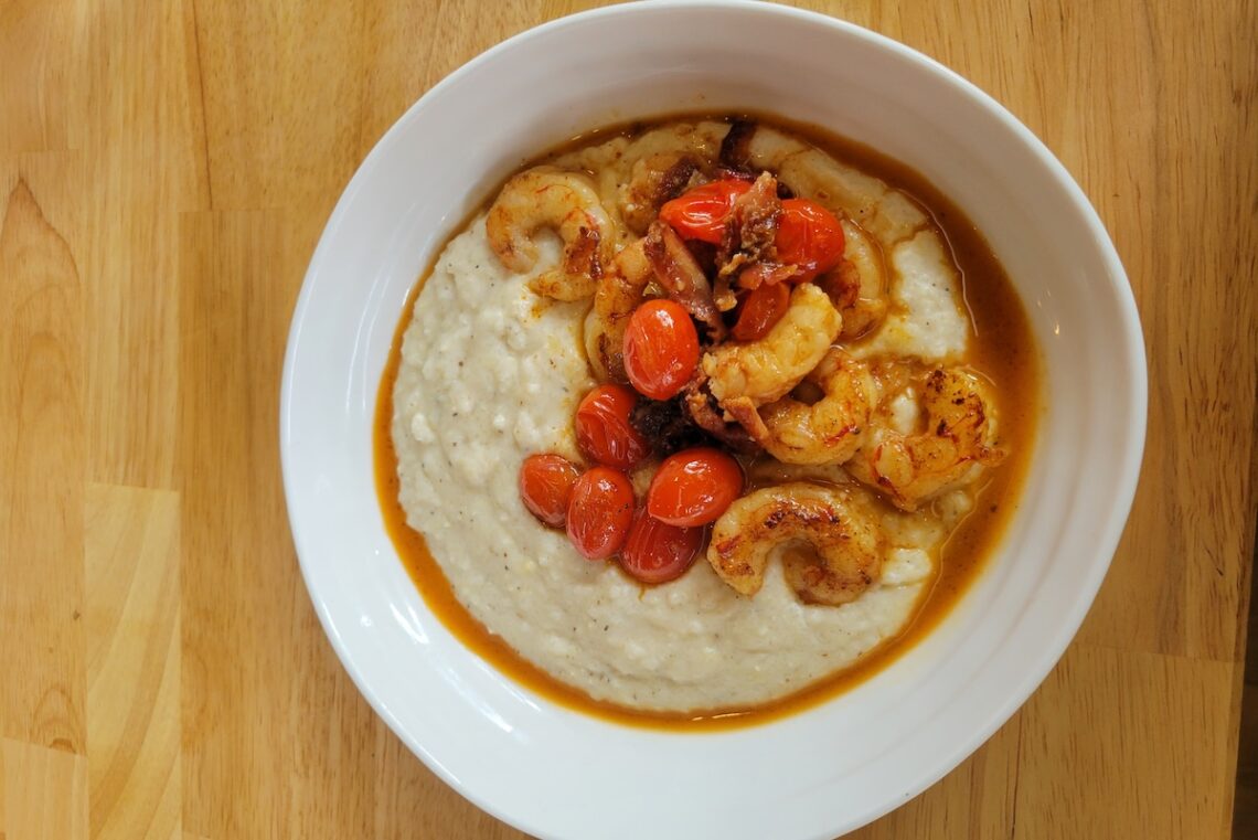 wood table with white bowl filled with shrimp and grits