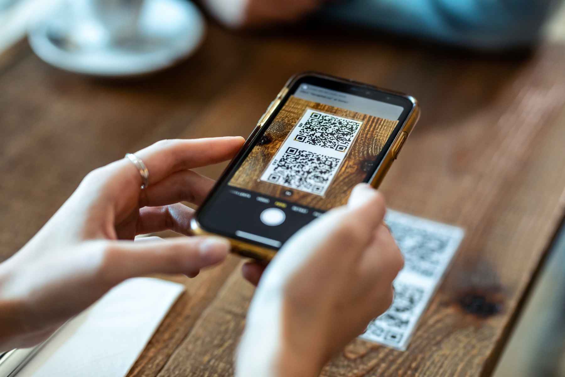 Close up on woman's hands using her phone to scan a QR code at a restaurant table for the menu.