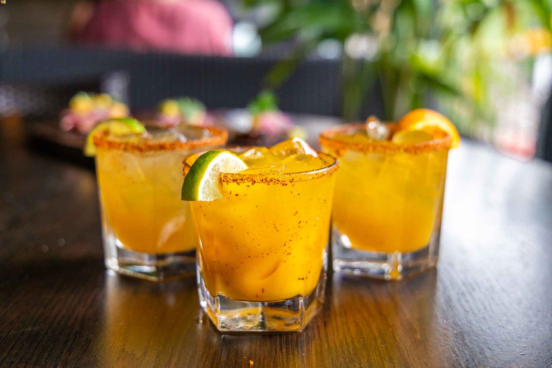 Bright orange ocktails in glasses rimmed with chile powder and garnished by lime and orange slices.