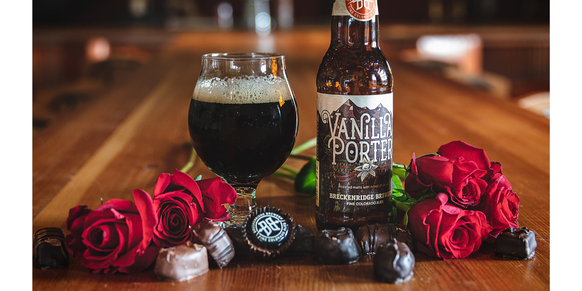 A bottle and glass of Breckenridge Brewery's Vanilla Porter on a wood table surrounded by roses and chocolates