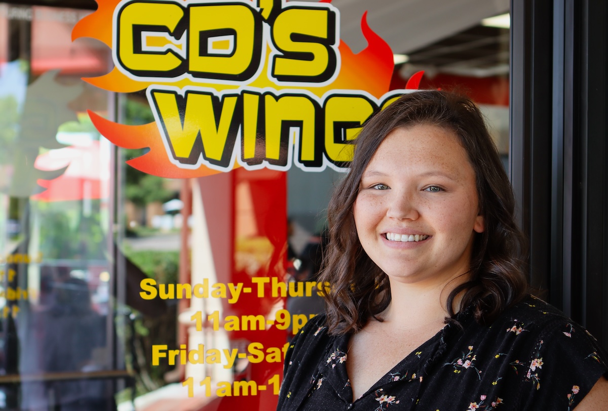 smiling woman with dark hair in front of colorful wing sign