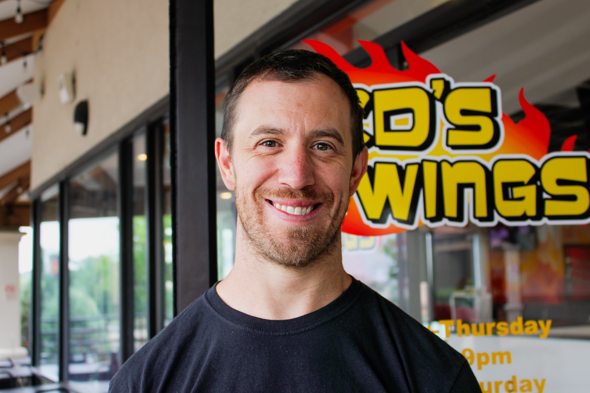 white man in front of colorful sign for wings