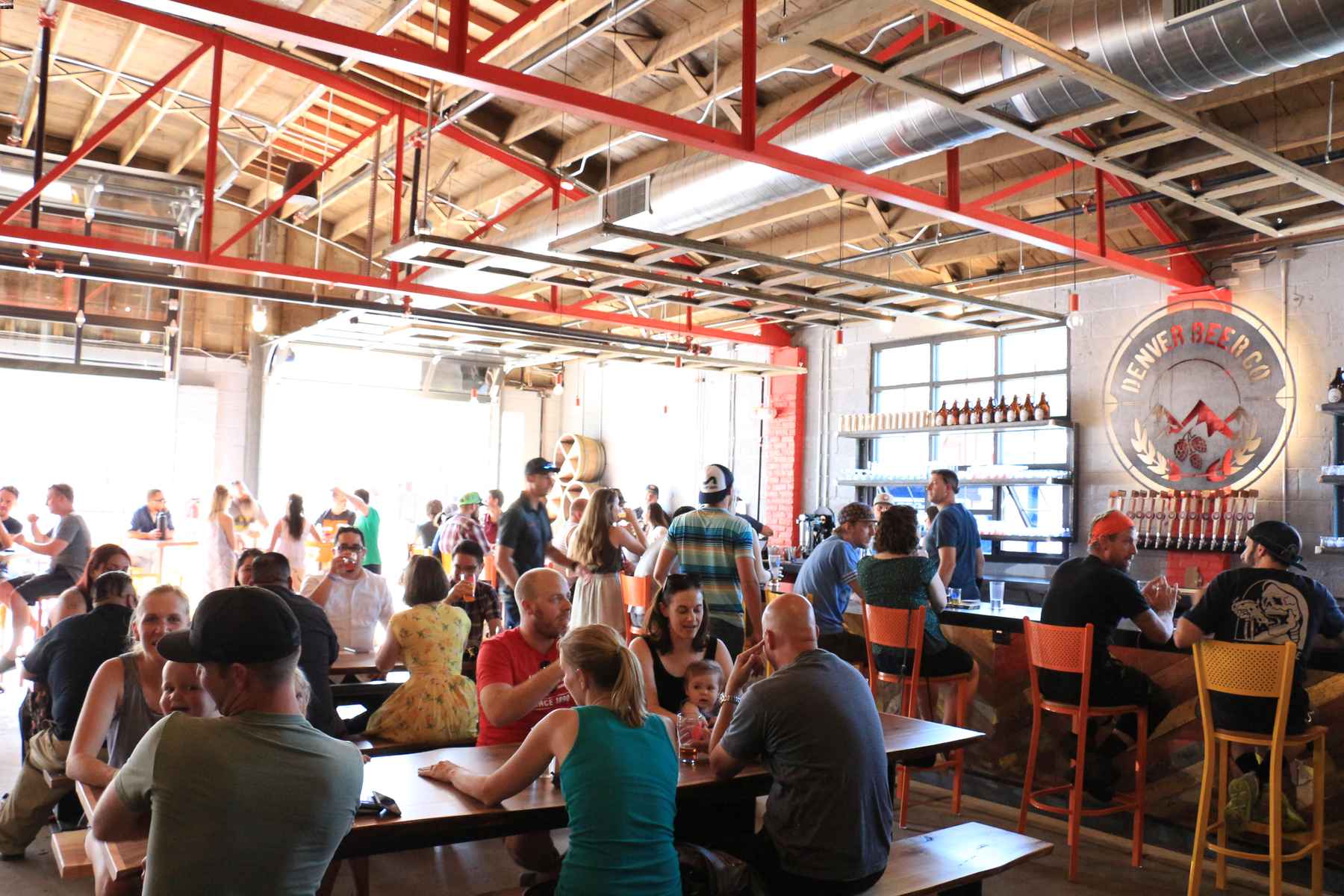 Interior of crowded Denver Beer Co. taproom with guests drinking at picnic tables and at the bar. DBC offered an NFT.