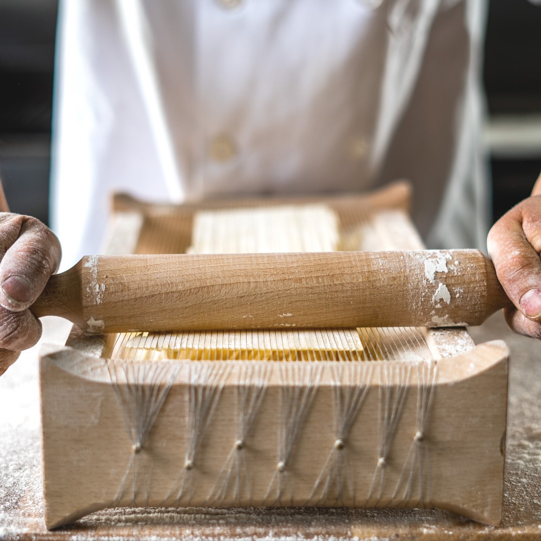 A chef makes pasta by hand using a rolling pin and other tools