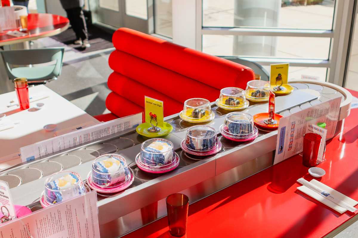 red booths with sushi in covered dishes on conveyor belt