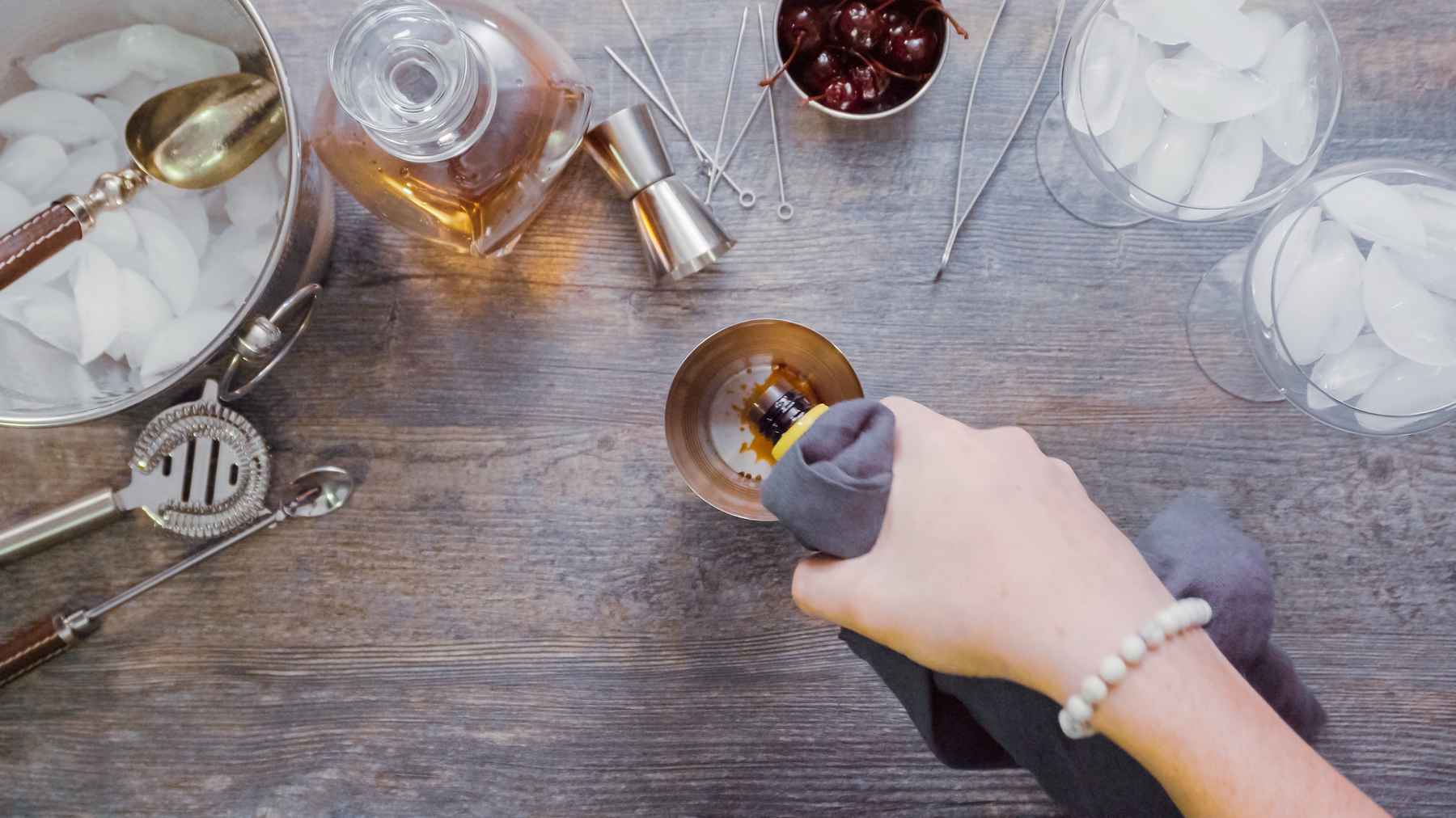 Overhead view of woman's hand adding bitters as she prepares a mixed drink.