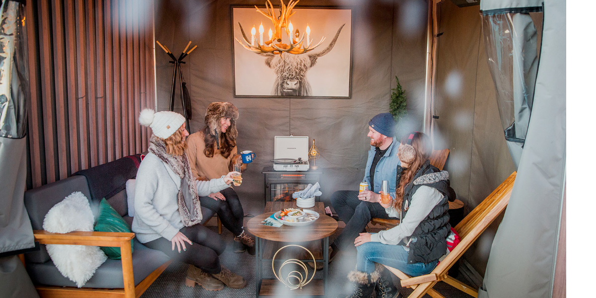 A group of four people dressed in sweaters and winter hats sits in a winter cabana at the Halcyon Hotel in Denver's Cherry Creek North neighborhood.