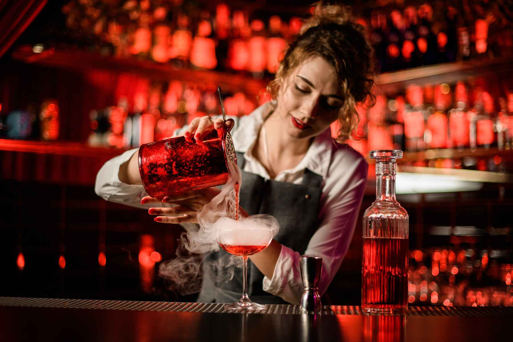 Young female bartender pouring a steaming liquid nitrogen cocktail into a glass. Quotes hospitality and bartending.