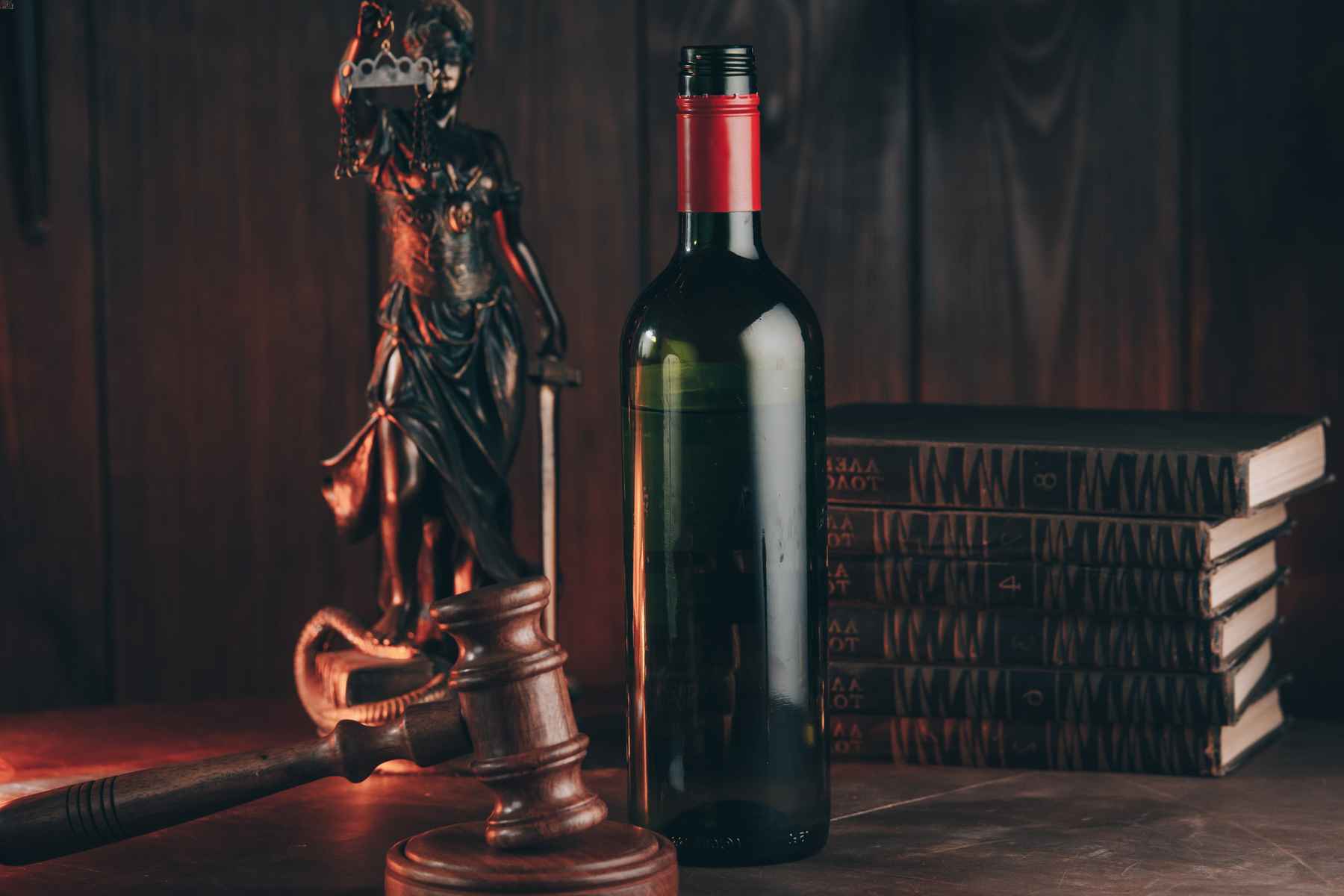 Lady justice statue and judical gavel next to a stack of law books and a bottle of wine. Liquor enforcement division.