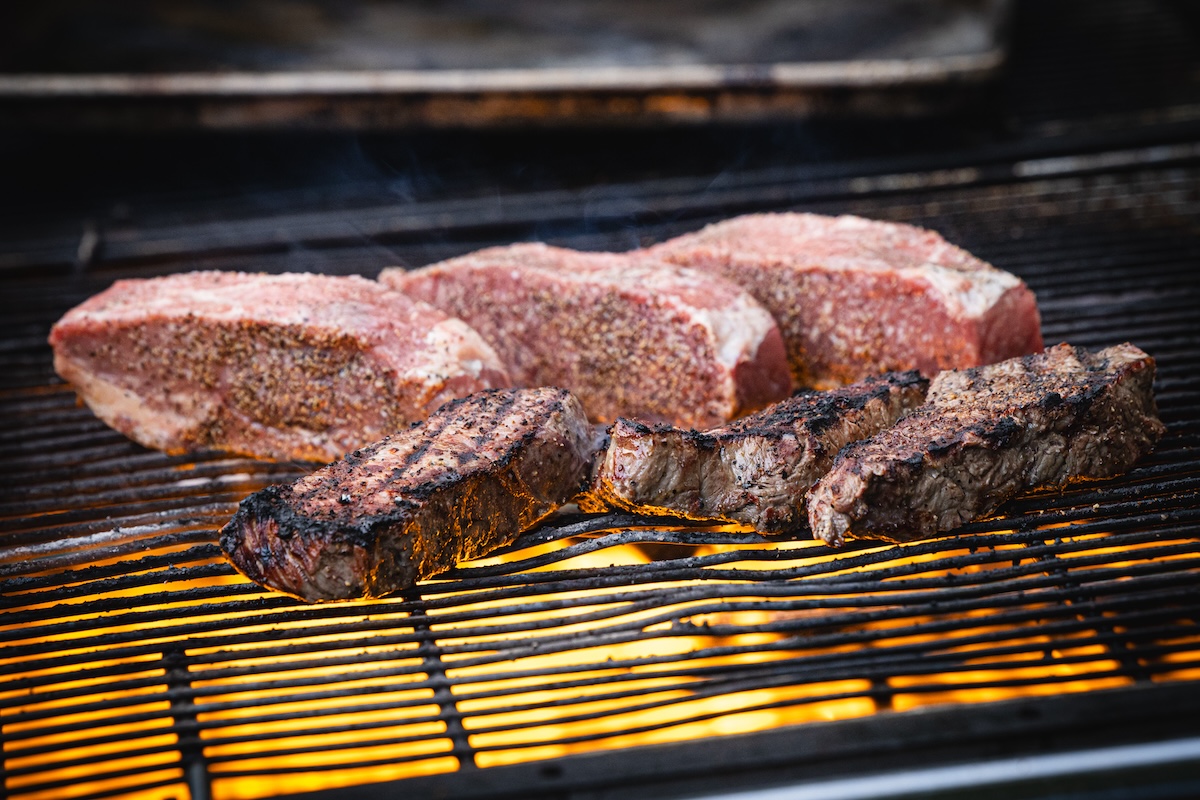 Beautiful strip steaks sizzling on the grill. | Photo by DiningOut Events