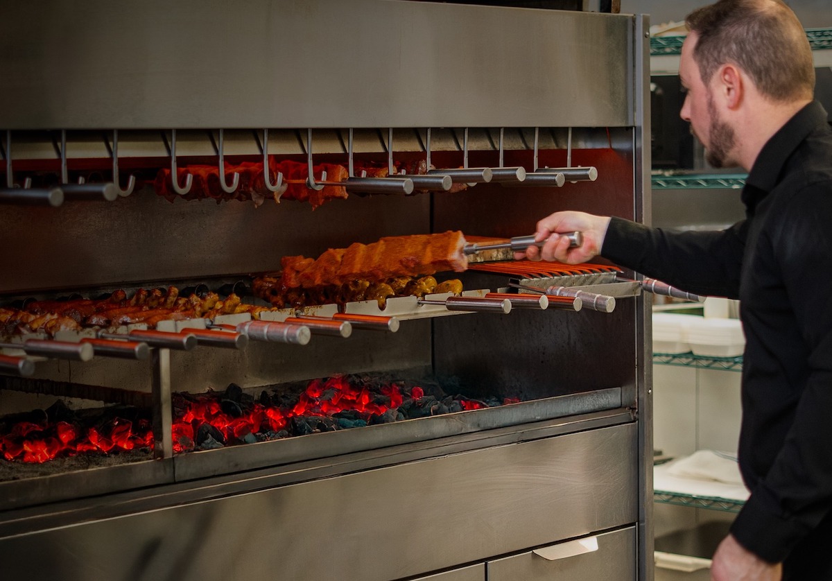Brasão Brazilian Steakhouse - DiningOut A gaucho tends the fire at Brasão Brazilian Steakhouse, where skewers of churrasco-roasted meats are carved tableside in true rodízio fashion. | Photo by Brasão Brazilian Steakhouse