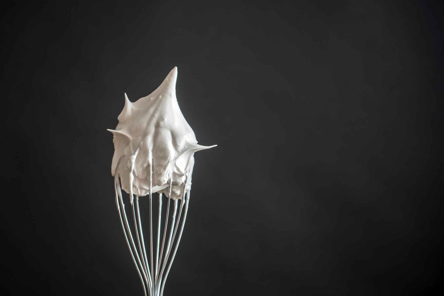 Upright metal whisk with cap of white egg whites on it.