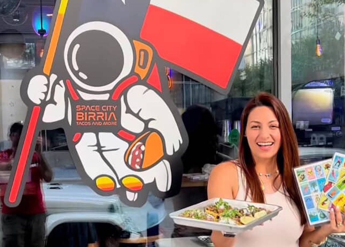 A loteria player posing with tacos and boards outside Space City Birria. | Photo by Space City Birria