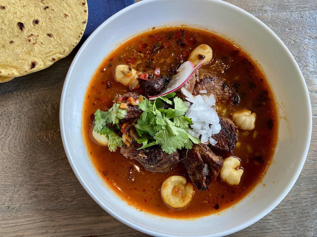 Birria, slow-roasted lamb marinated in chile adobo wrapped in a banana leaf, consommé, onion, and cilantro with corn tortillas at Caracol. | Photo by H-Town Restaurant Group