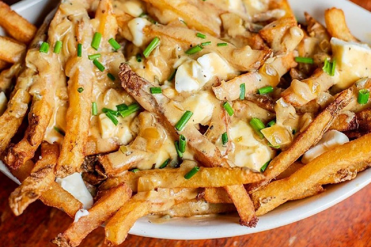 City O’ City’s vegan poutine topped with golden fries, savory mushroom gravy, melty cashew ricotta, and fresh chives, served in a white bowl.