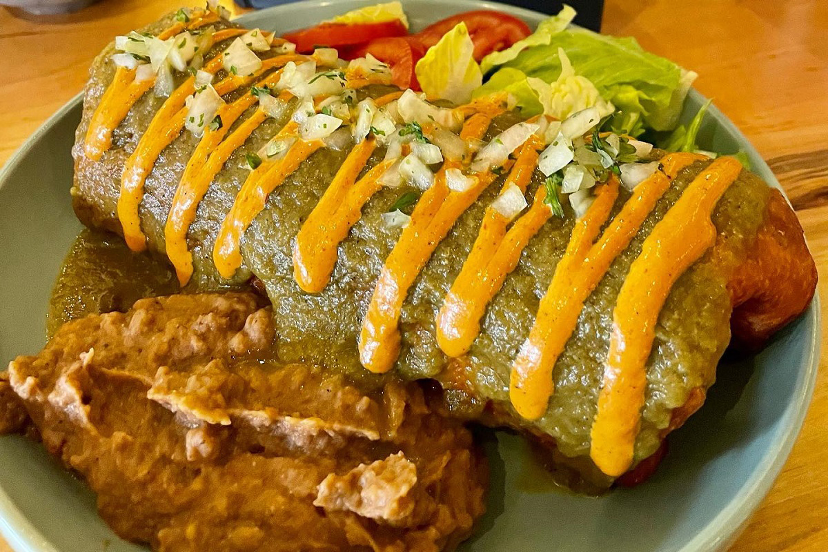Smothered burrito at Fellow Traveler in Denver, topped with green chile, orange sauce, and diced onions, served with refried beans and a side salad.