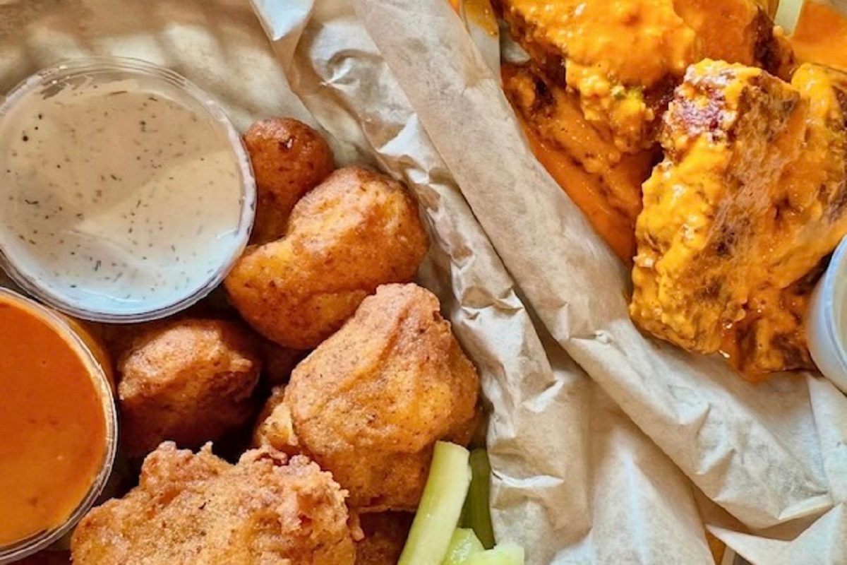 Buffalo sauced seitan wings, fried cauliflower, dipping sauces, and pickle spears served on parchment at Fire on the Mountain in Denver.