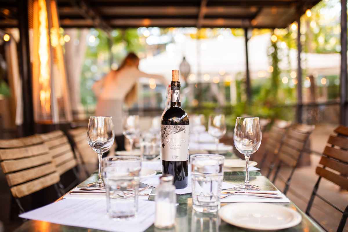 - DiningOut Hand pouring Strongwater mixer Signature Sparkling tonic into large cocktail glass garnished with cucumber, dill, and lemon.