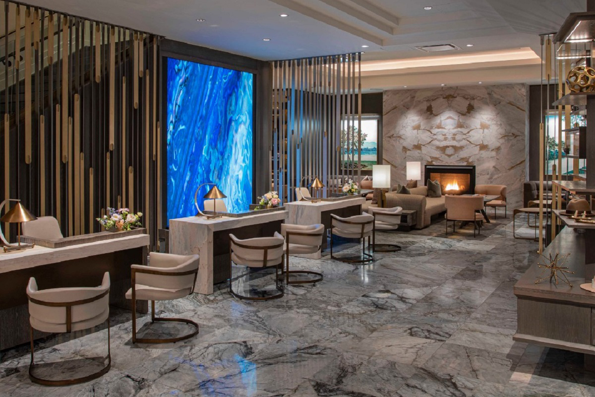Hotel Clio’s lobby in Denver featuring marble floors, a glowing blue art wall, fireplace seating, and modern desks with gold-accented lighting.

