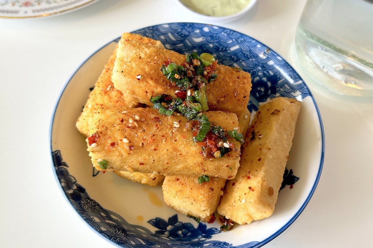 Crispy mala tofu bars topped with spicy scallion-chili sauce, served in a blue patterned bowl at MAKfam in Denver with a side of creamy green dipping sauce.
