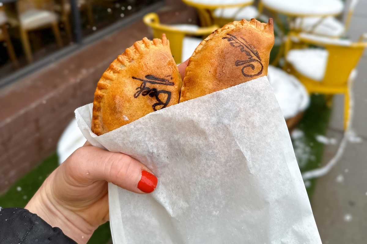 - DiningOut hand holding empanadas in a paper bag