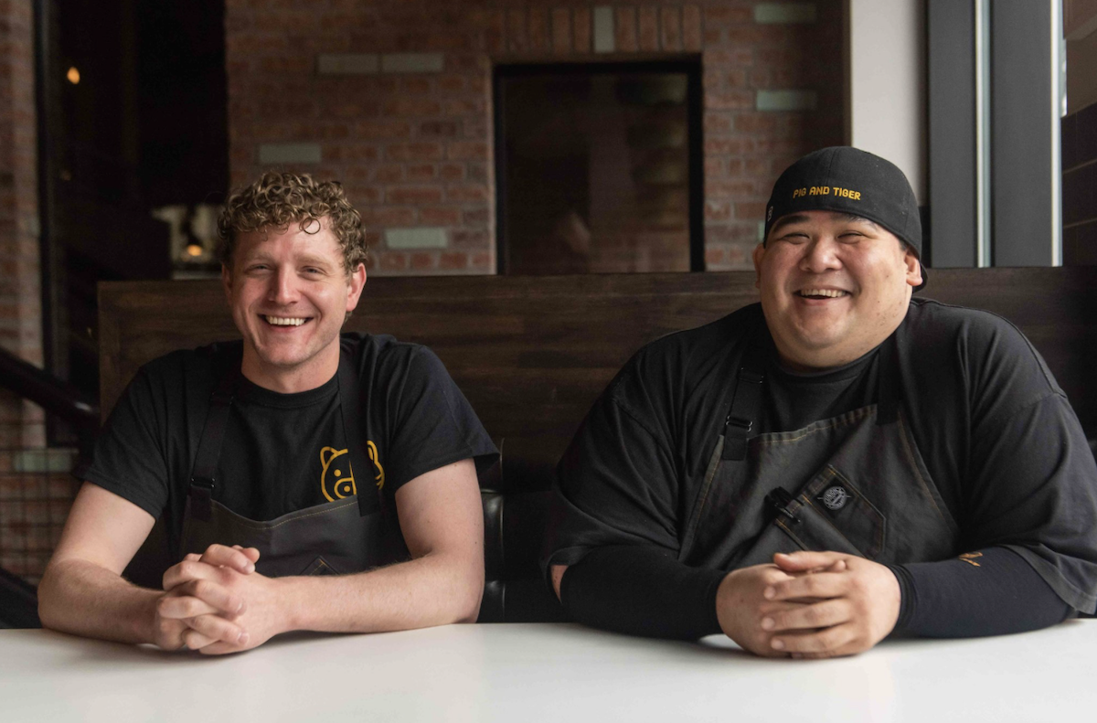two men sitting at white table with brick background
