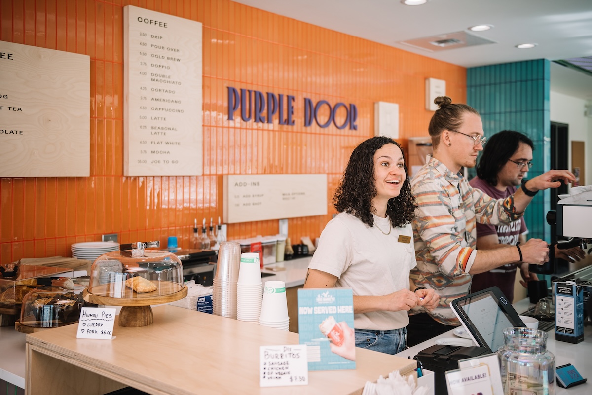baristas making coffee in front of orange wall