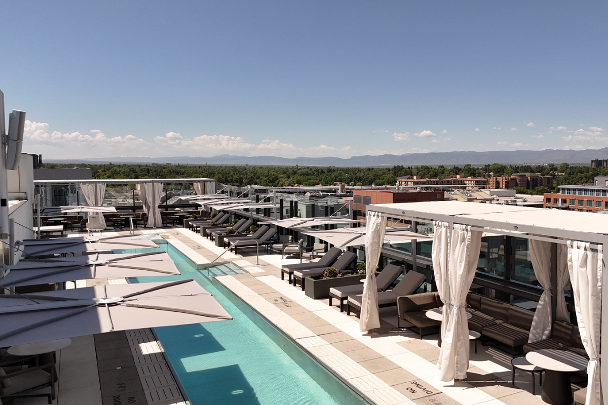 Rooftop pool deck at The Jacquard in Denver, with lounge chairs, shaded cabanas, and mountain views on a clear day.