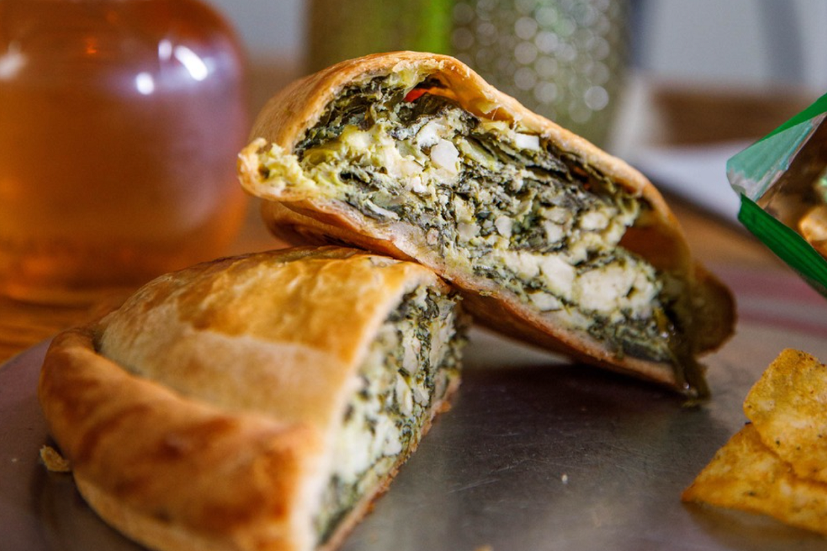 Spinach and cheese empanada with a golden crust, cut in half to show the filling at The Pasty Republic in Denver.