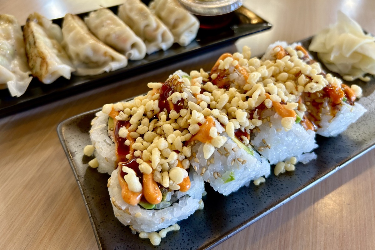 Crispy-topped sushi rolls drizzled with spicy mayo and eel sauce, served with pickled ginger and gyoza on the side at Wellness Sushi in Denver.