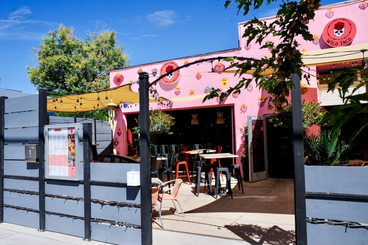 Wild Taco Berkeley’s bright pink exterior features heart murals and outdoor seating with string lights, colorful chairs, and a shaded patio area.