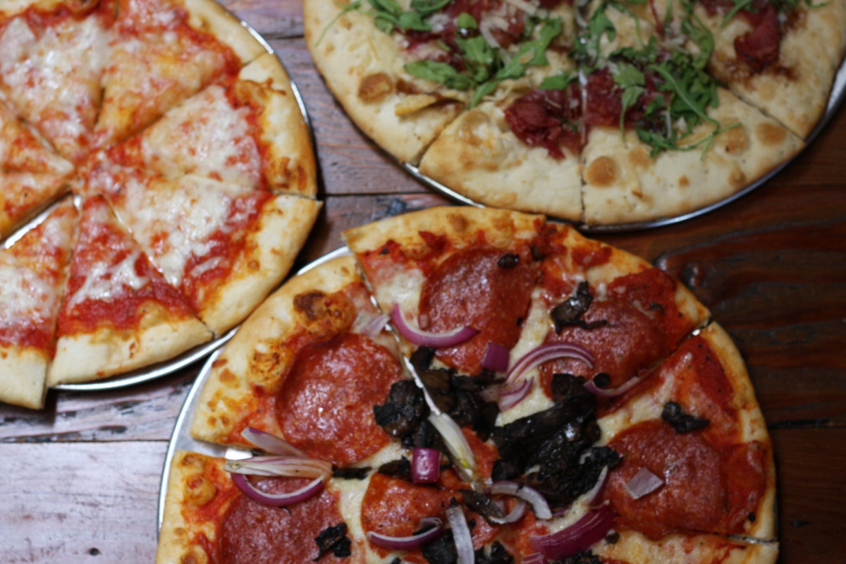 Three pizzas topped with cheese, pepperoni, mushrooms, red onion, arugula, and cured meats at Blackbird Public House in Denver.