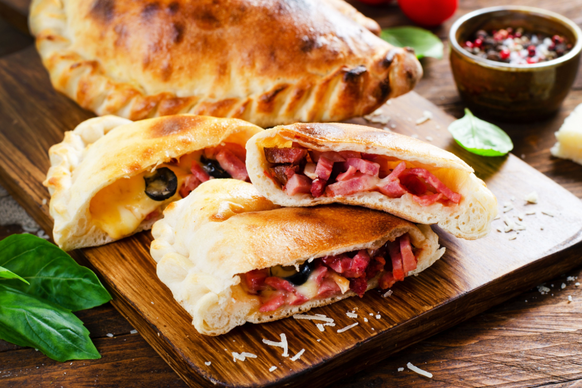 - DiningOut Delicious Pizza Calzone, Traditional Italian Pizza Stuffed with Ham and Cheese with Tomatoes and Fresh Basil on Wooden Background