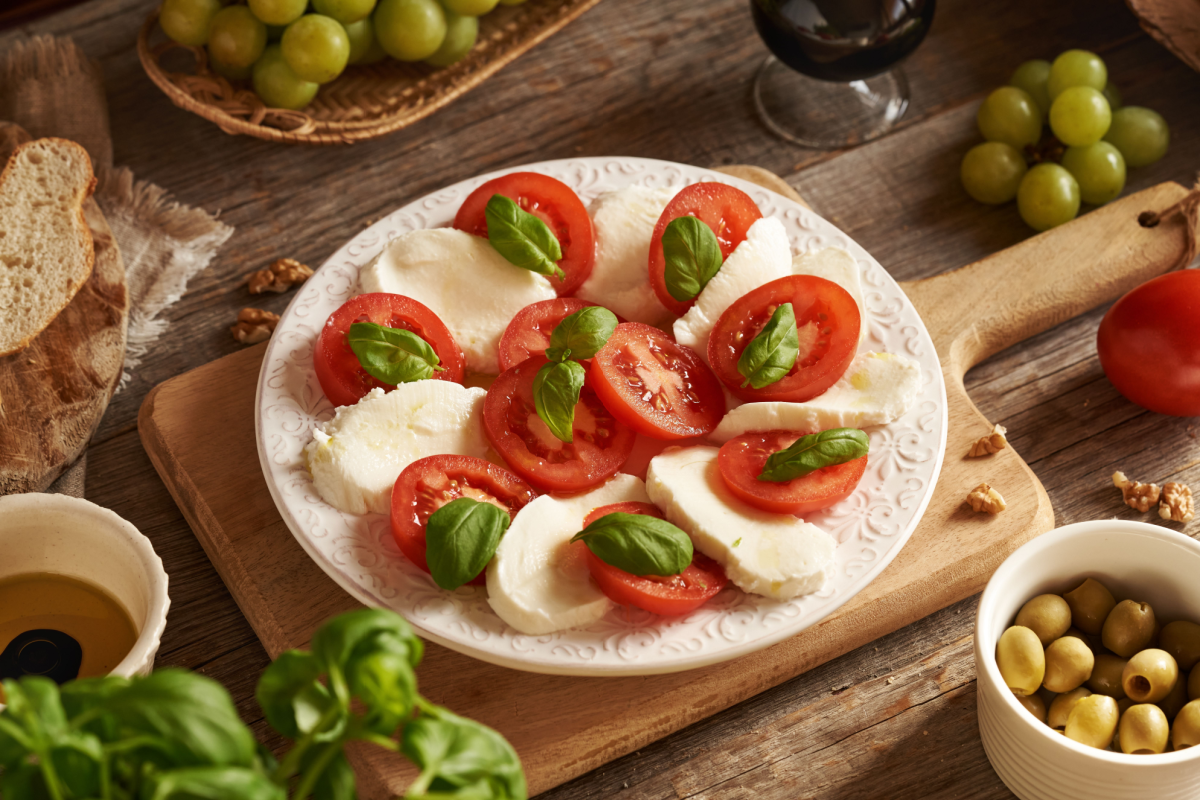 - DiningOut Italian Caprese salad - tomatoes, mozzarella cheese and fresh basil leaves, with green olives, grapes, ciabatta and balsamic vinegar on a table