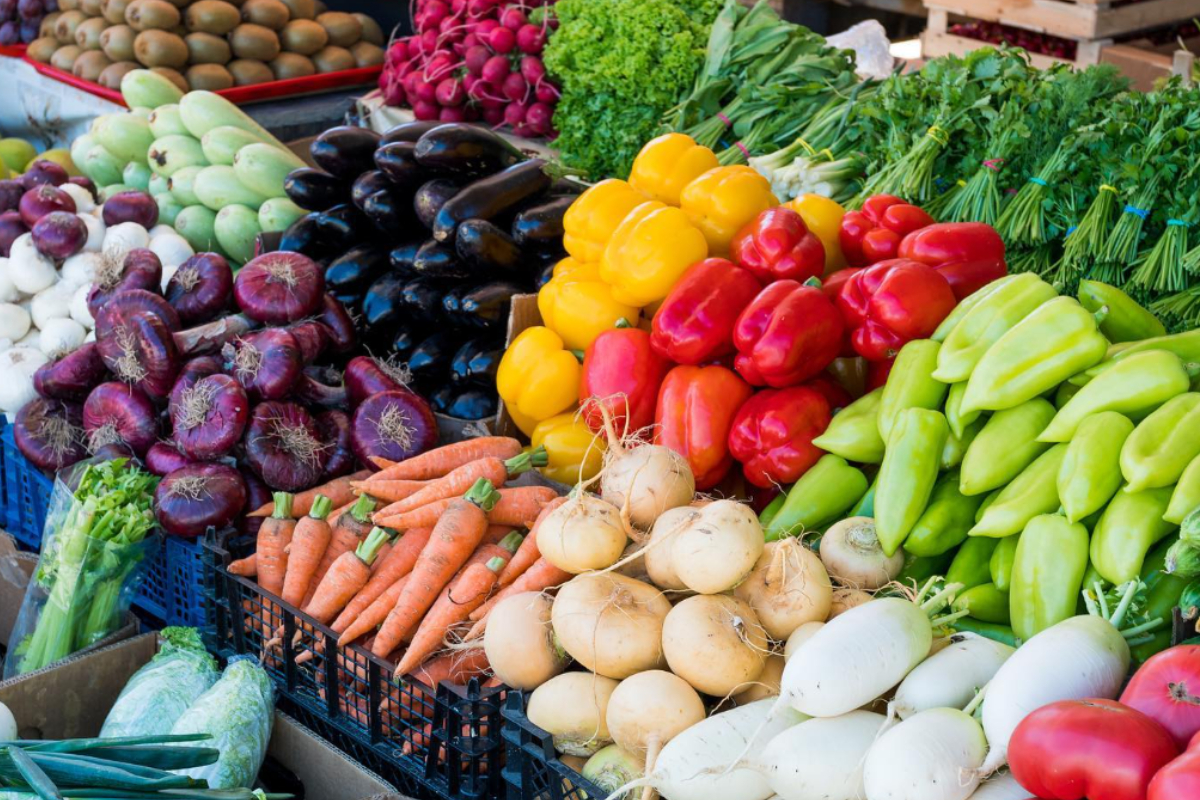 Colorful vegetables including bell peppers, carrots, onions, eggplants, and radishes neatly stacked at Central Park Farmers Market in Denver, Colorado.