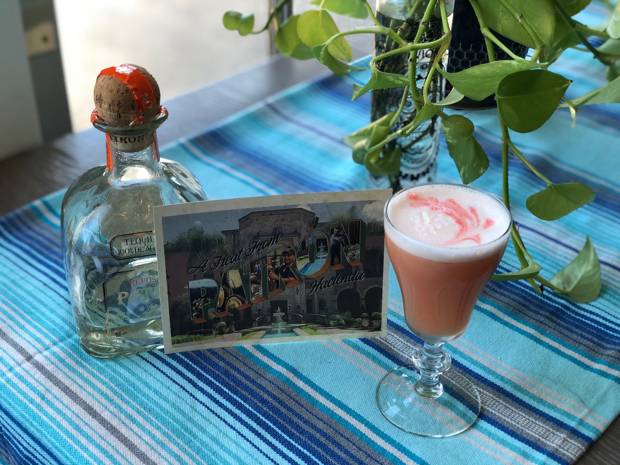 Pink cocktail next on bright blue tablecloth next to tequila bottle for Cocktail Creators.