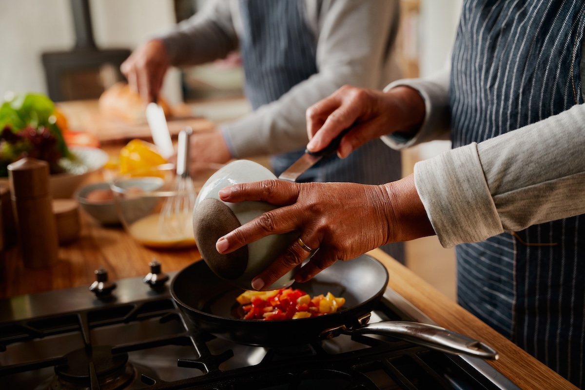 Hands of multi-cultural elderly couple cooking healthy breakfast together in modern kitchen at stove