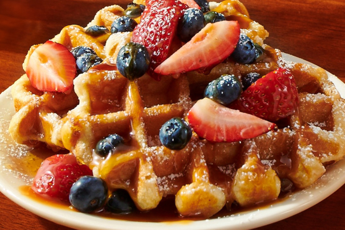 Liège waffle topped with fresh strawberries, blueberries, powdered sugar, and caramel drizzle at Denny's in Denver.
