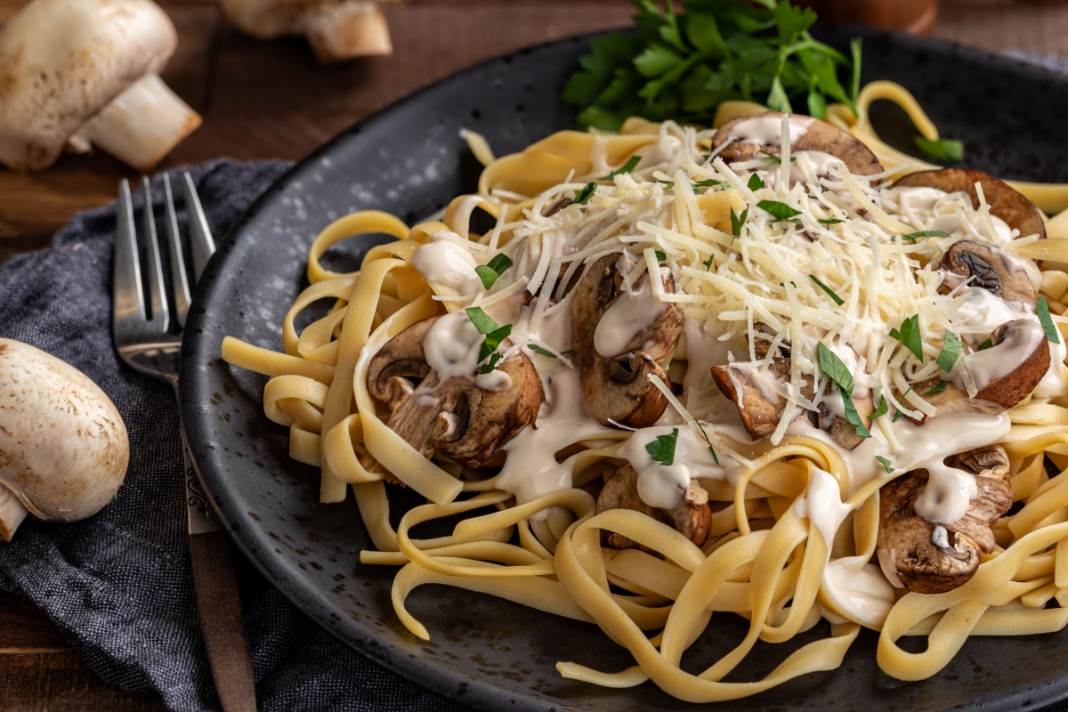 - DiningOut Creamy fettuccine alfredo with mushrooms and shredded parmesan cheese on a black plate. Closeup view