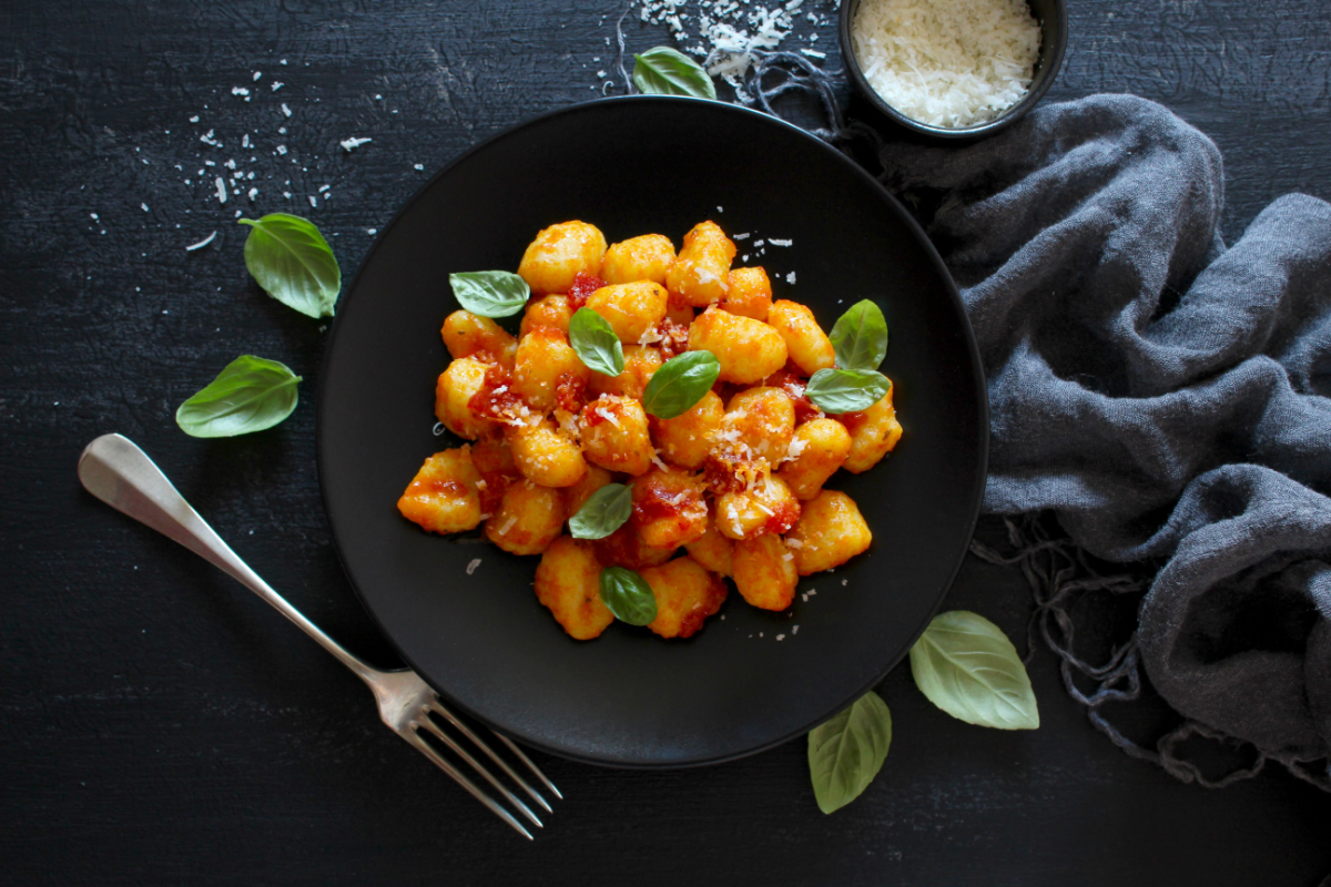 - DiningOut Traditional Italian potato gnocchi with tomato sauce, parmesan cheese and fresh basil on dark table. Top view. Vegetarian and vegan food.